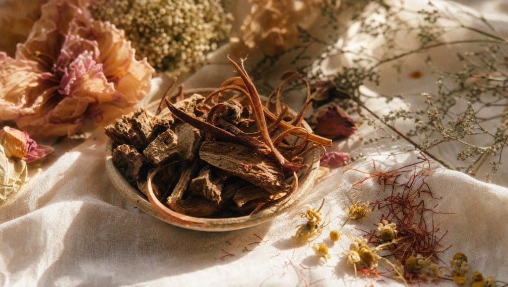 Écorce séchée de griffe de chat dans une coupe, sur un drap de lin clair, entourée de fleurs séchées et de pistils de safran