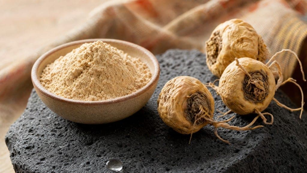 Poudre de maca en bol et racines séchées sur roche volcanique sombre