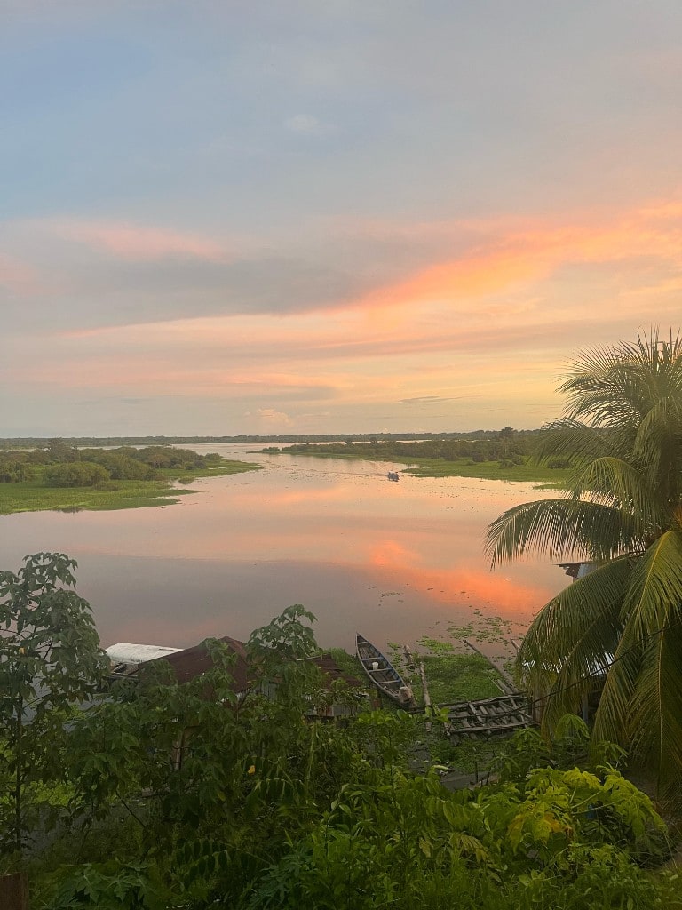 Amazonie, au crépuscule — Le ciel orangé se reflète sur l'eau calme — une pirogue amarrée, la jungle au loin.